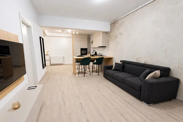 Open-plan living room with a grey sofa, a dining table with green chairs and the kitchen behind, at Casa del Mar, Mamaia Nord