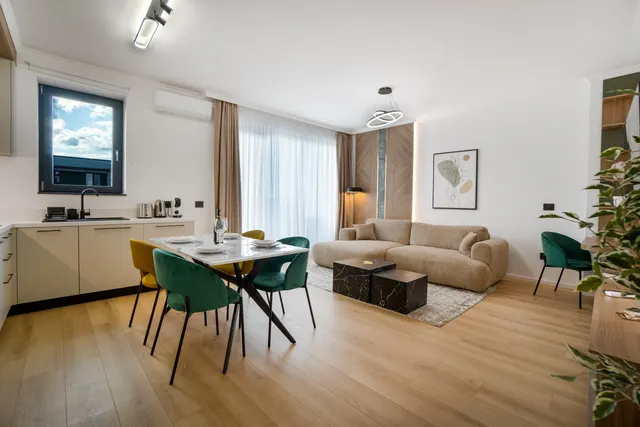 Open-plan living room with a beige sofa, a dining table with green chairs and a kitchen, at Coresi, Brașov