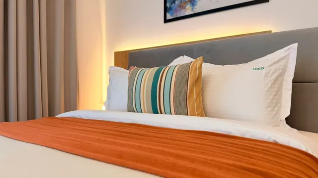 Bed with a striped cushion, an orange throw and a softly lit headboard, at Icon Studio, București