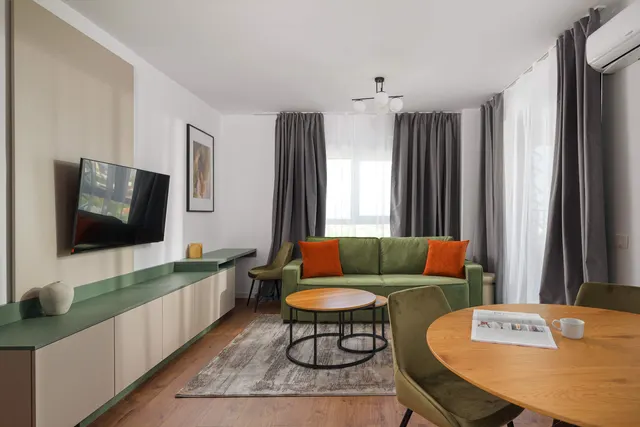 Living room with a green sofa, a wall-mounted TV and a round table, at City of Mara, Timișoara