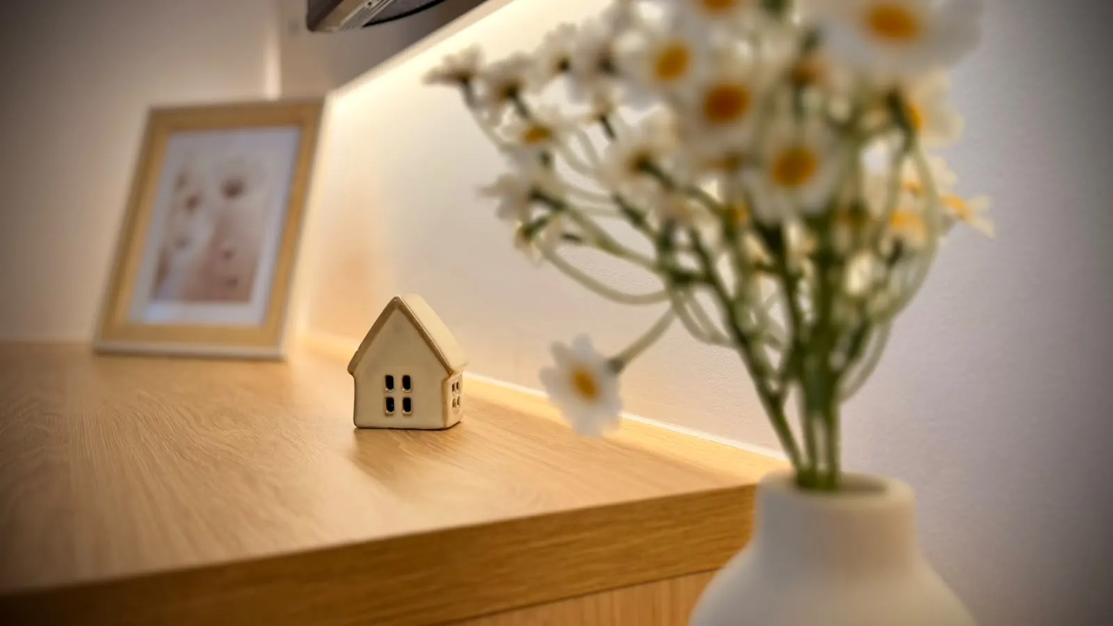 A small wooden house and a vase of daisies on a shelf, in a HUBIX Renting apartment